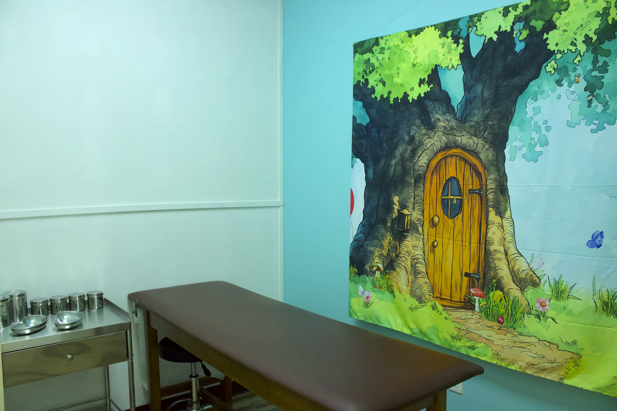 Exam room with a storybook tree mural and tiny wooden door